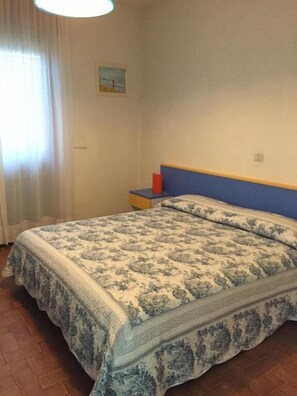 A bedroom with a bed, a nightstand, a red object on the nightstand, and a painting on the wall.
