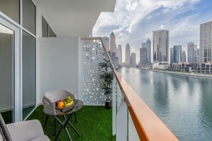 A balcony with a city view, a chair, a table with fruit, and a decorative panel. - Gogoto Lux Studio Canal & Burj View (Dubai)