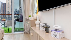 A modern living room with a large window, a sofa, a small table with fruits, and a massage gun on the counter.