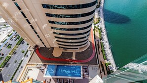 Un immeuble de grande hauteur à la façade incurvée, un espace piscine agrémenté d’un logo bleu et une promenade en bord de mer.