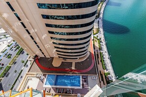 A high-rise building with a curved facade, a pool area with a blue logo, and a waterfront promenade. - Gogoto Lux Studio Canal & Burj View (Dubai)