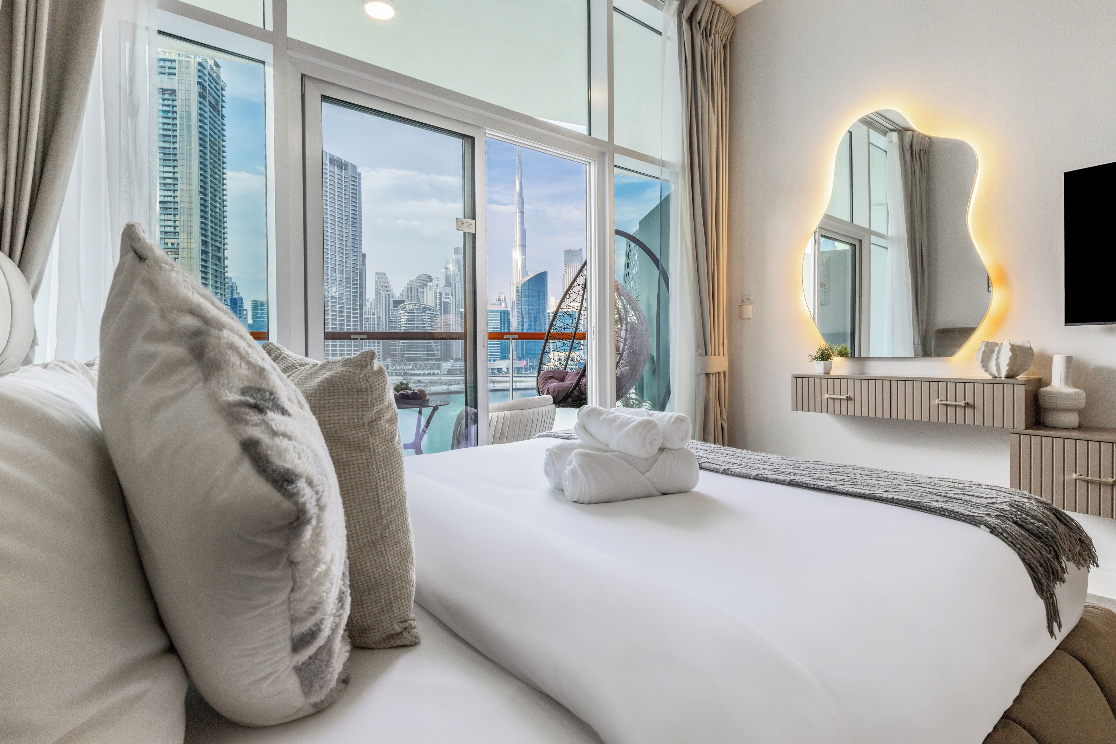Een moderne hotelkamer met een groot bed, uitzicht over de stad, een ronde spiegel en een wandtv.
