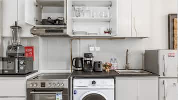 Uma cozinha compacta com forno embutido, cafeteira, máquina de lavar e pia.