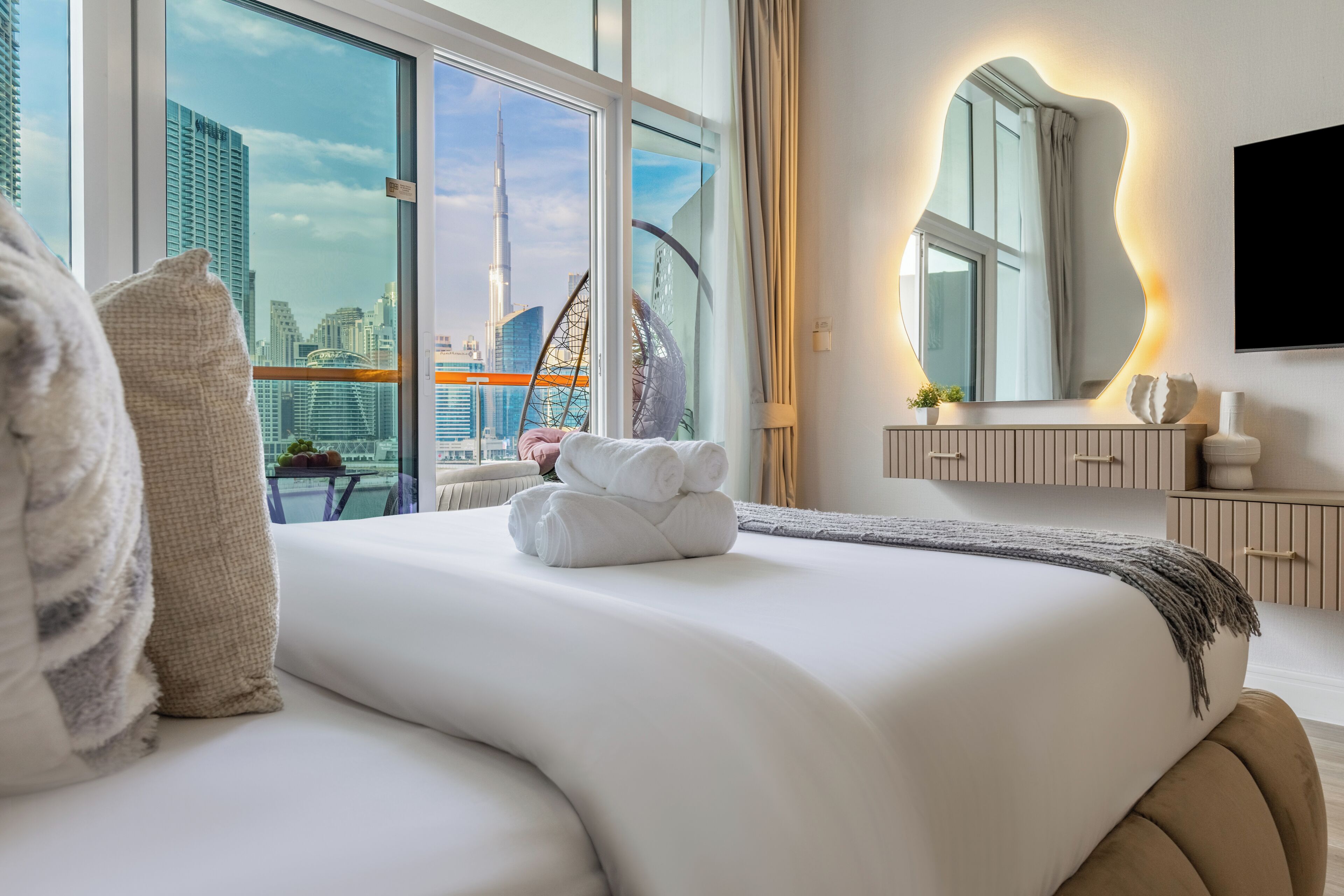 Quarto de hotel moderno com uma cama grande, vista para a cidade, um espelho amplo e uma televisão de tela plana.