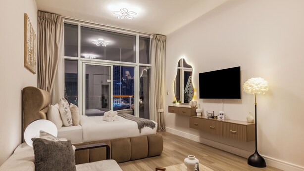 A modern bedroom with a large window, a flat-screen TV, a bedside table, and a sofa. - Gogoto6 Premium Studio Burj Khalifa & Canal View (Dubai)
