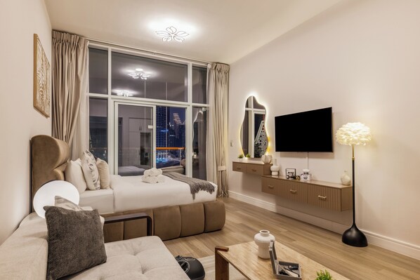 A modern bedroom with a large window, a flat-screen TV, a bedside table, and a sofa.