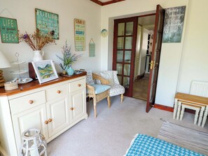 Une pièce chaleureuse avec une commode en bois, une chaise en osier et une table à manger agrémentée d’un vase de fleurs.