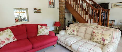 A living room with a red sofa, a plaid sofa, a staircase, and a window with a view.