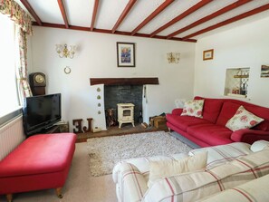 Un salon avec une cheminée, un canapé rouge, un téléviseur et une horloge au mur.