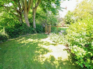 A garden with a wooden gate, lush greenery, and a clear sky. - Tan-y-ffordd Cottage (Llandudno Junction)