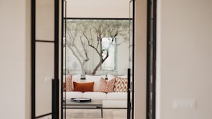 A modern living room with a sofa, patterned cushions, a coffee table, and a view of trees through a glass door. - Exclusive villa with pool, near Noto - DiCasaInSicilia (Noto)