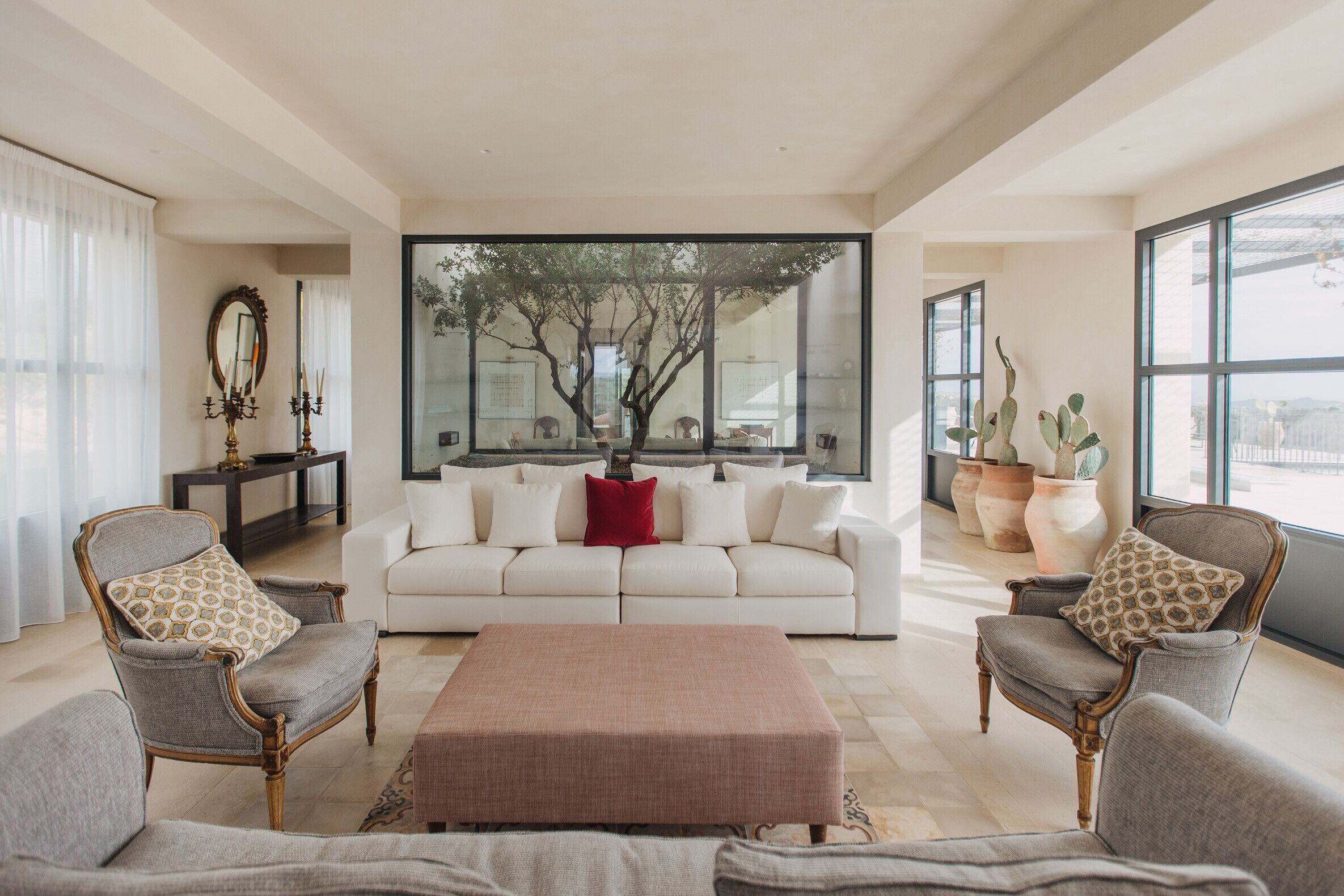 A living room with a white sofa, two armchairs, a coffee table, and a large window with a view of trees.