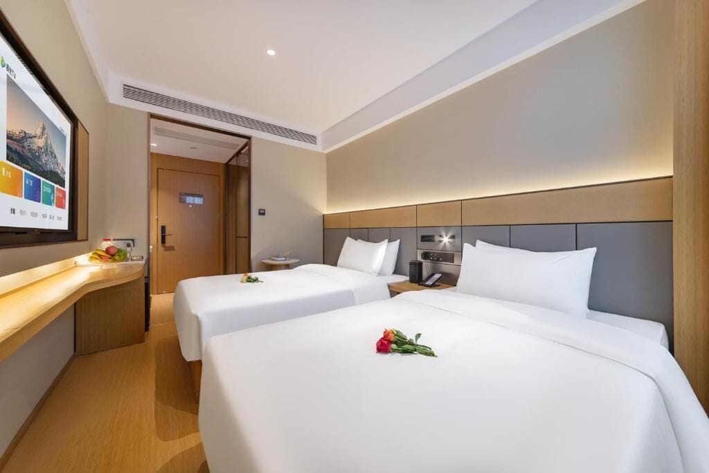 Una camera d'albergo con due letti, una TV, un tavolino e una porta in legno.