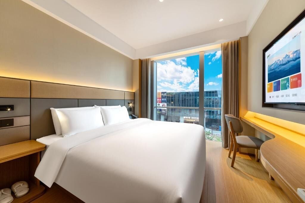 Une chambre d’hôtel avec un grand lit, un bureau, une chaise et un téléviseur fixé au mur.