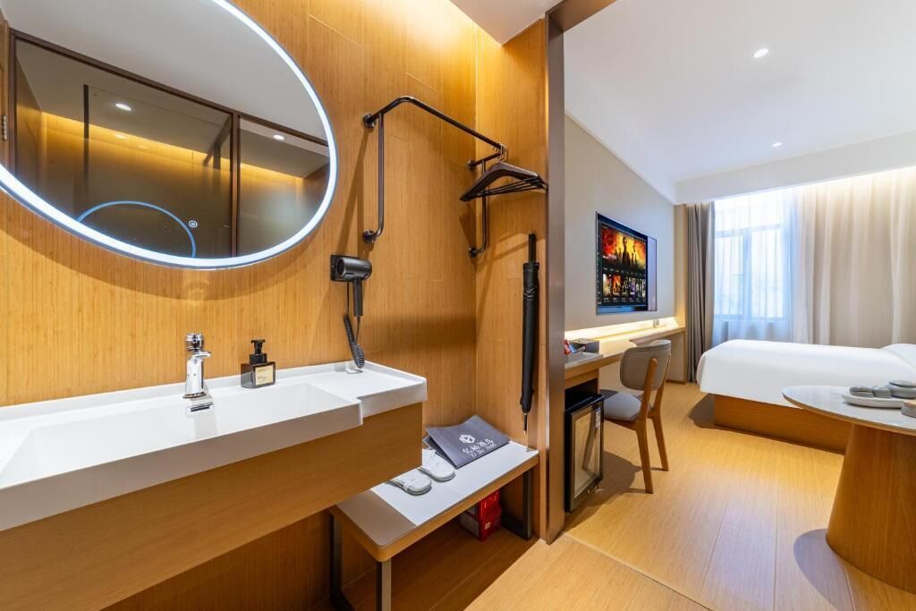 Ein modernes Hotelzimmer mit Holzvertäfelung, einem großen Spiegel, einem Schreibtisch mit Stuhl, einem Bett und einem Fernseher.