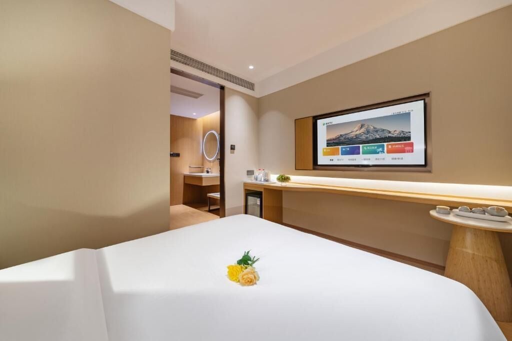 Une chambre d’hôtel avec un lit, un téléviseur fixé au mur, une petite table avec un vase et un miroir.