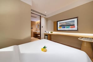 A hotel room with a bed, a TV mounted on the wall, a small table with a vase, and a mirror.