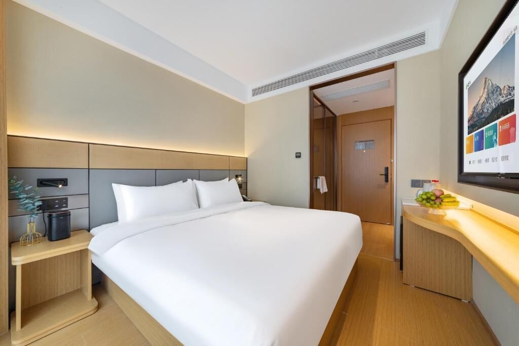 A modern hotel room with a large bed, bedside tables, a small desk, and a mounted TV.