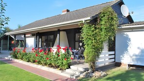 Ein Gebäude mit überdachter Terrasse, Außenbestuhlung und einem Garten mit roten Blumen.
