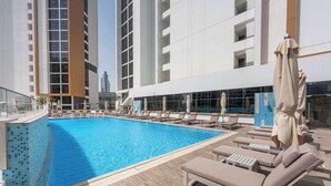 Una piscina al terrat amb gandules i ombrelles, envoltada d'edificis moderns.