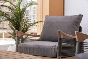 A wicker chair with a grey cushion, a potted plant, and a view of buildings through a window. - Free housekeeping visits during your stay - StayShort - Chic Modern Studio That Sleeps 3 at Riviera Beachfront (Meydan)