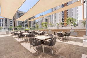 An outdoor patio area with tables and chairs, a grill, and a view of high-rise buildings. - Free housekeeping visits during your stay - StayShort - Chic Modern Studio That Sleeps 3 at Riviera Beachfront (Meydan)