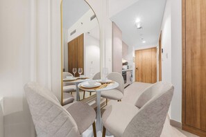 A modern dining area with a round table, chairs, and a kitchen in the background. - Free housekeeping visits during your stay - StayShort - Chic Modern Studio That Sleeps 3 at Riviera Beachfront (Meydan)