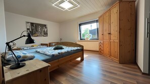 Un dormitorio con cama de madera, un escritorio con lámpara, un radiador y una ventana con vistas.