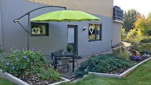 Ein modernes Haus mit Terrasse, Tisch, Stühlen und einem leuchtend grünen Sonnenschirm.