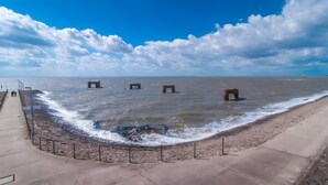 Une promenade en bord de mer, avec une barrière en béton, une plage de sable et un ciel bleu dégagé.