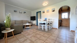 Un salon comprenant un canapé, une table basse, un téléviseur et un coin repas avec des chaises et une table.