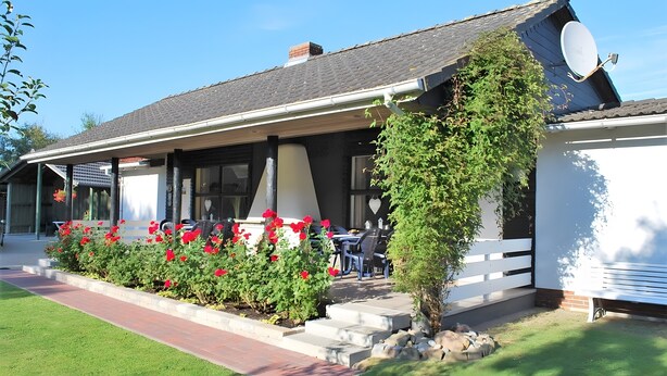 Un bâtiment doté d’un patio couvert, d’un espace extérieur aménagé pour s’asseoir et d’un jardin avec des fleurs rouges.