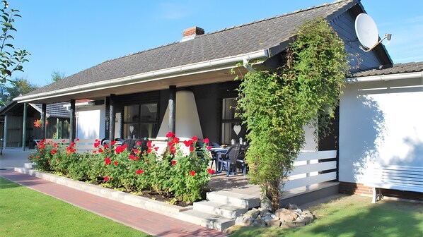 Ein Gebäude mit überdachter Terrasse, Außenbestuhlung und einem Garten mit roten Blumen.