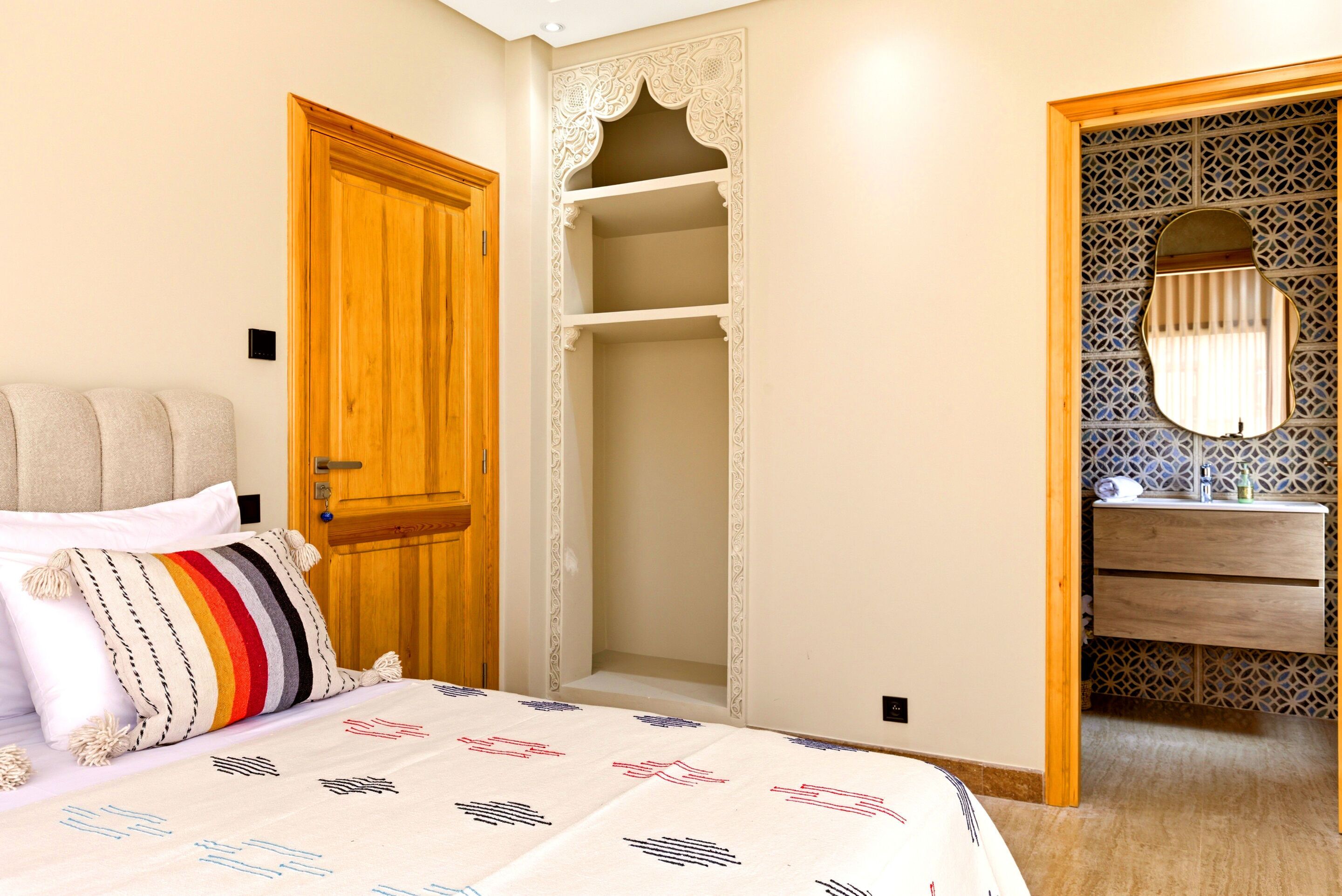 A bedroom with a bed, a wooden door, a wardrobe, and a bathroom with a mirror.