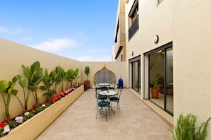 A patio with a table and chairs, surrounded by potted plants and a decorative wall.