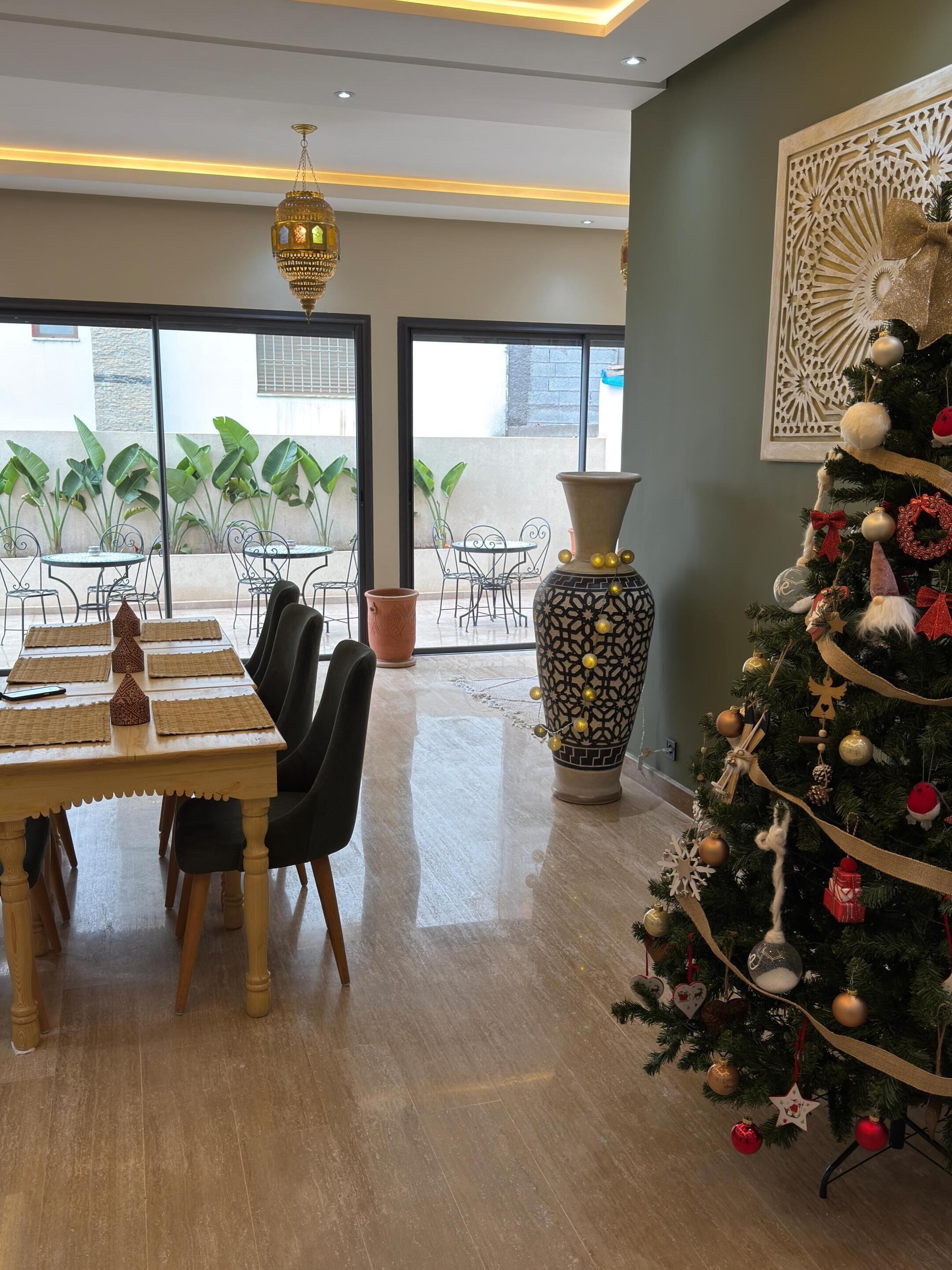 A dining area with a table, chairs, a large vase, and a decorated Christmas tree.
