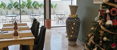 A dining area with a table, chairs, a large vase, and a decorated Christmas tree.