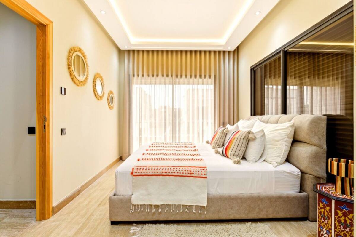 Un dormitorio con cama, sofá, ventana grande con cortinas y decoración en las paredes.