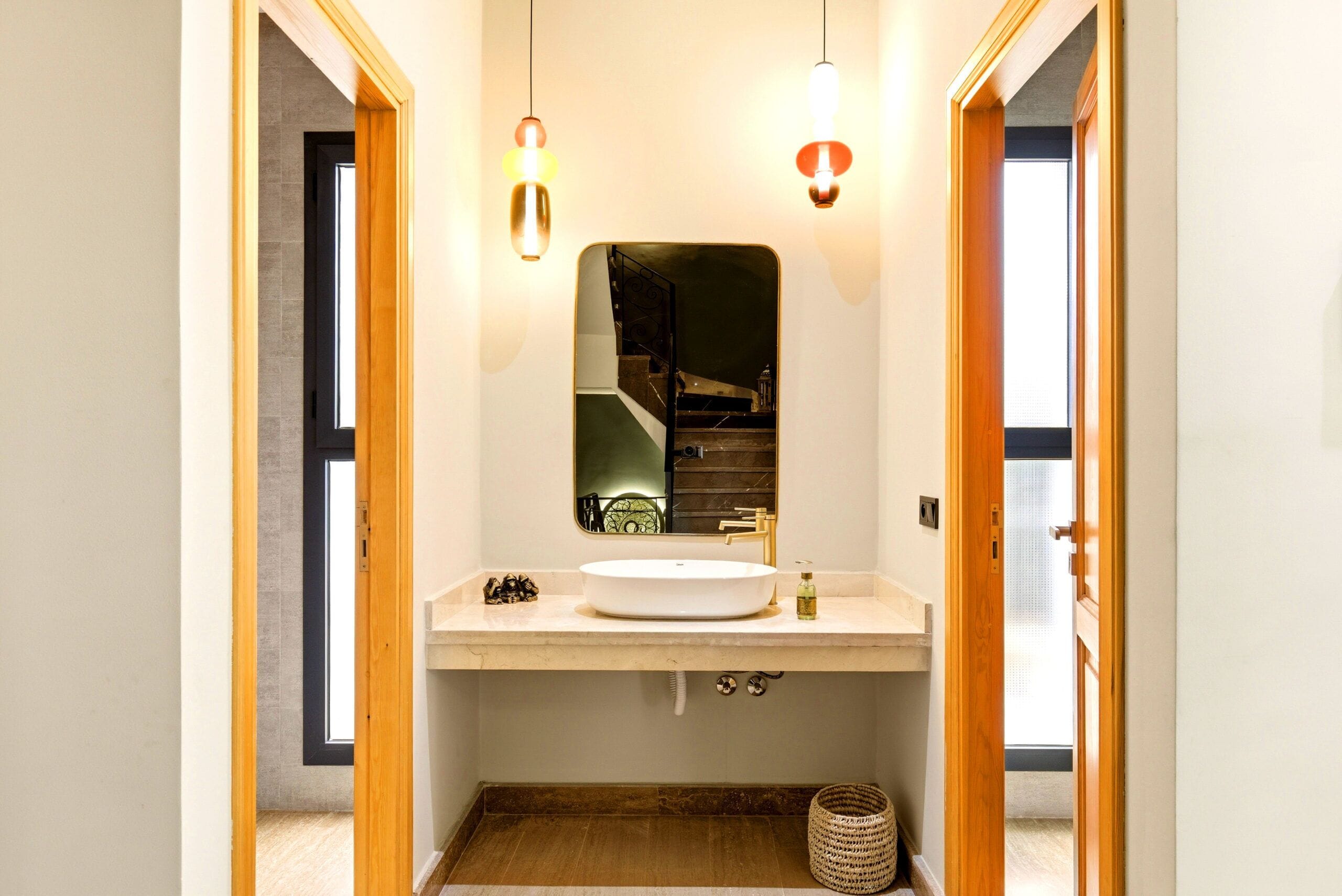 A modern bathroom with a large mirror, a round sink, and two pendant lights.
