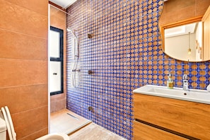 Une salle de bain avec un mur carrelé, un lavabo, un miroir et une douche.