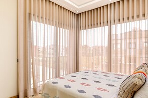 A hotel room with a bed, a window with curtains, and a view of buildings outside. - Riad Villa Alain (Deroua)