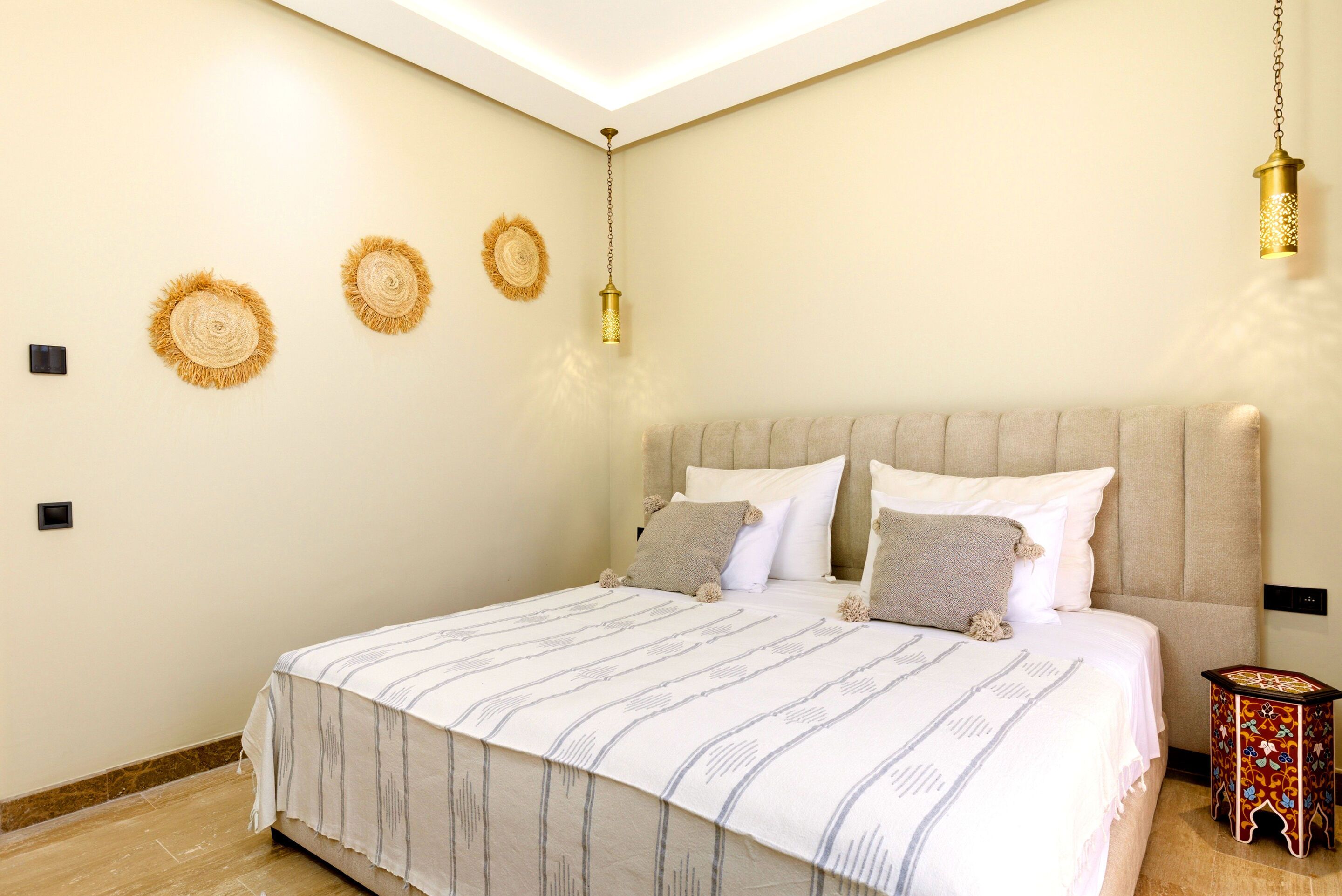 A bedroom with a bed, headboard, wall-mounted lamps, and a small side table.