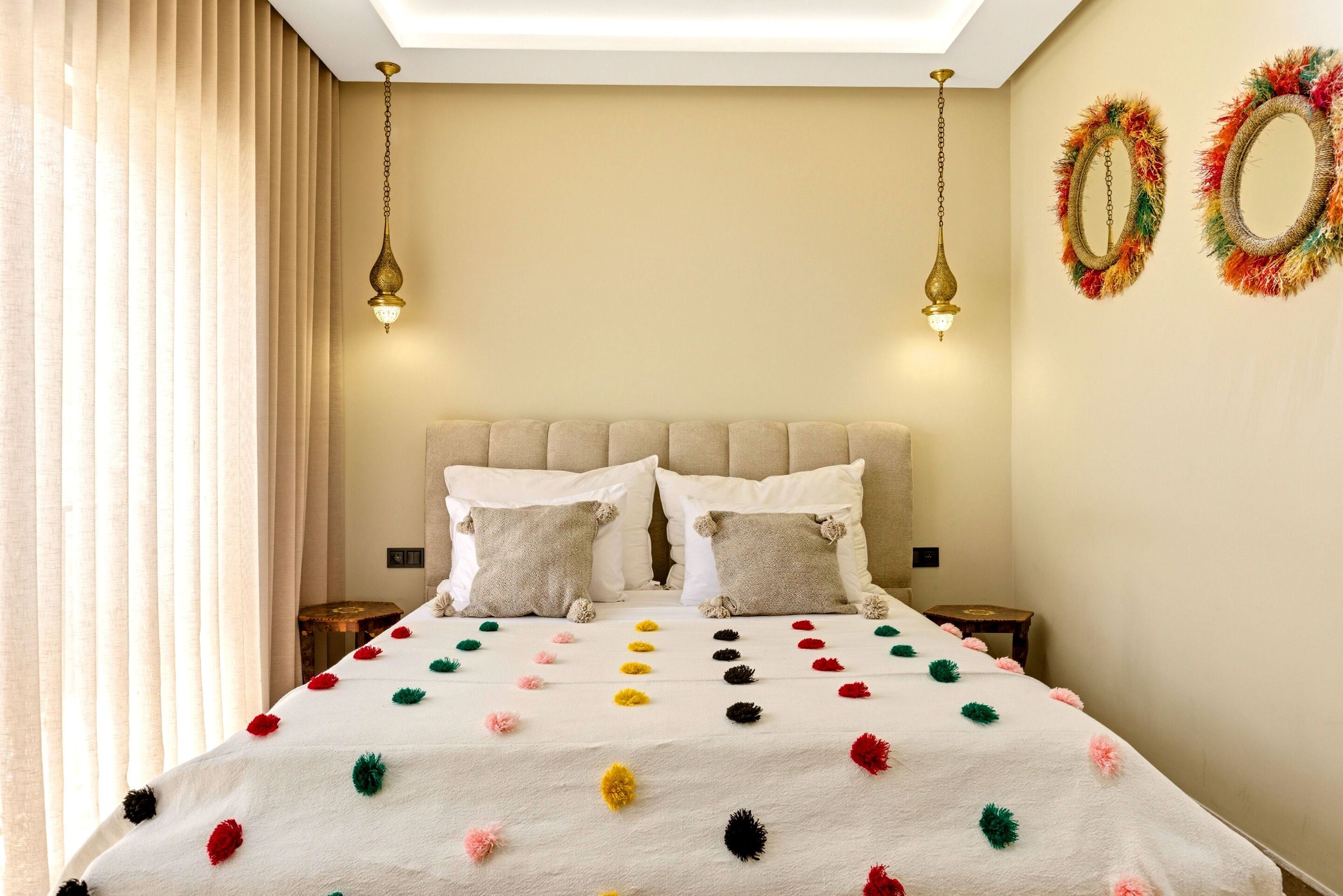Un dormitorio con una cama, dos mesitas de noche, una lámpara en el techo y espejos decorativos en la pared.