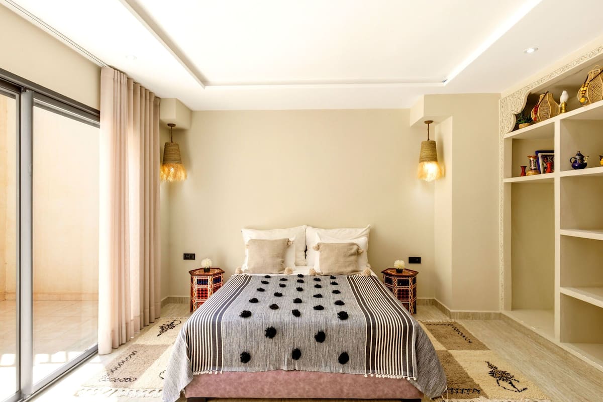Un dormitorio con una cama grande, dos mesitas de noche, una estantería y un ventanal corredero.