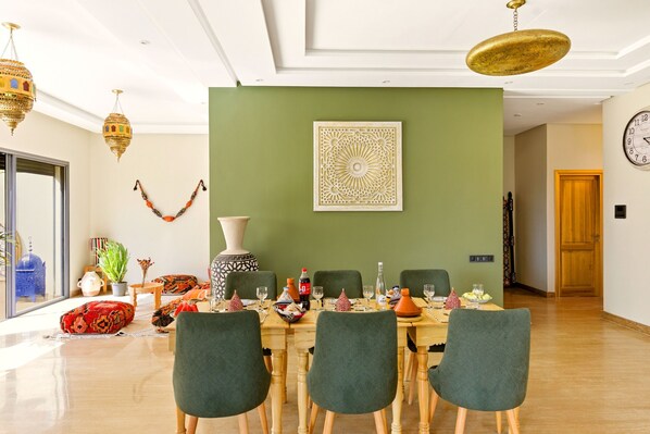 A dining area with a green wall, a decorative wall piece, and a wooden table set for six.