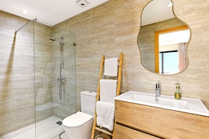 A modern bathroom with a glass shower enclosure, a white toilet, a wooden vanity with a sink, and a mirror with a unique frame.