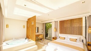 Ett modernt hotellrum med en stor säng, ett separat badrum med jacuzzi, ett skrivbord och utsikt över grönområden utanför.