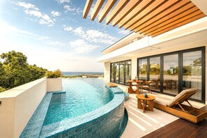 A modern infinity pool with a curved edge, a wooden deck, and outdoor seating. - Zen Hillside Oceanview Bali (Badung)