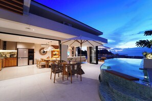 A modern kitchen with a dining area, a large umbrella, and a pool. - Zen Hillside Oceanview Bali (Badung)