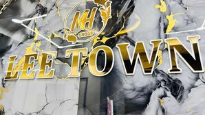 Een marmeren muur met 'LEE TOWN' en 'MH GROUP' logo's.